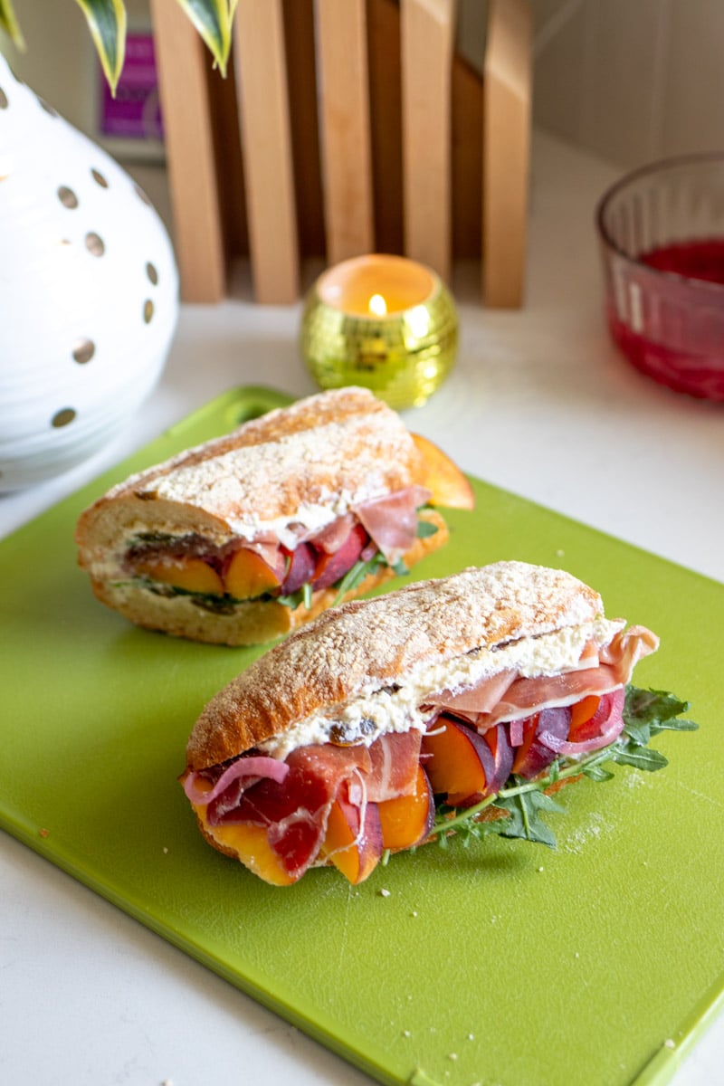 two halves of a a prosciutto, peach and feta sandwich on a green cutting board.