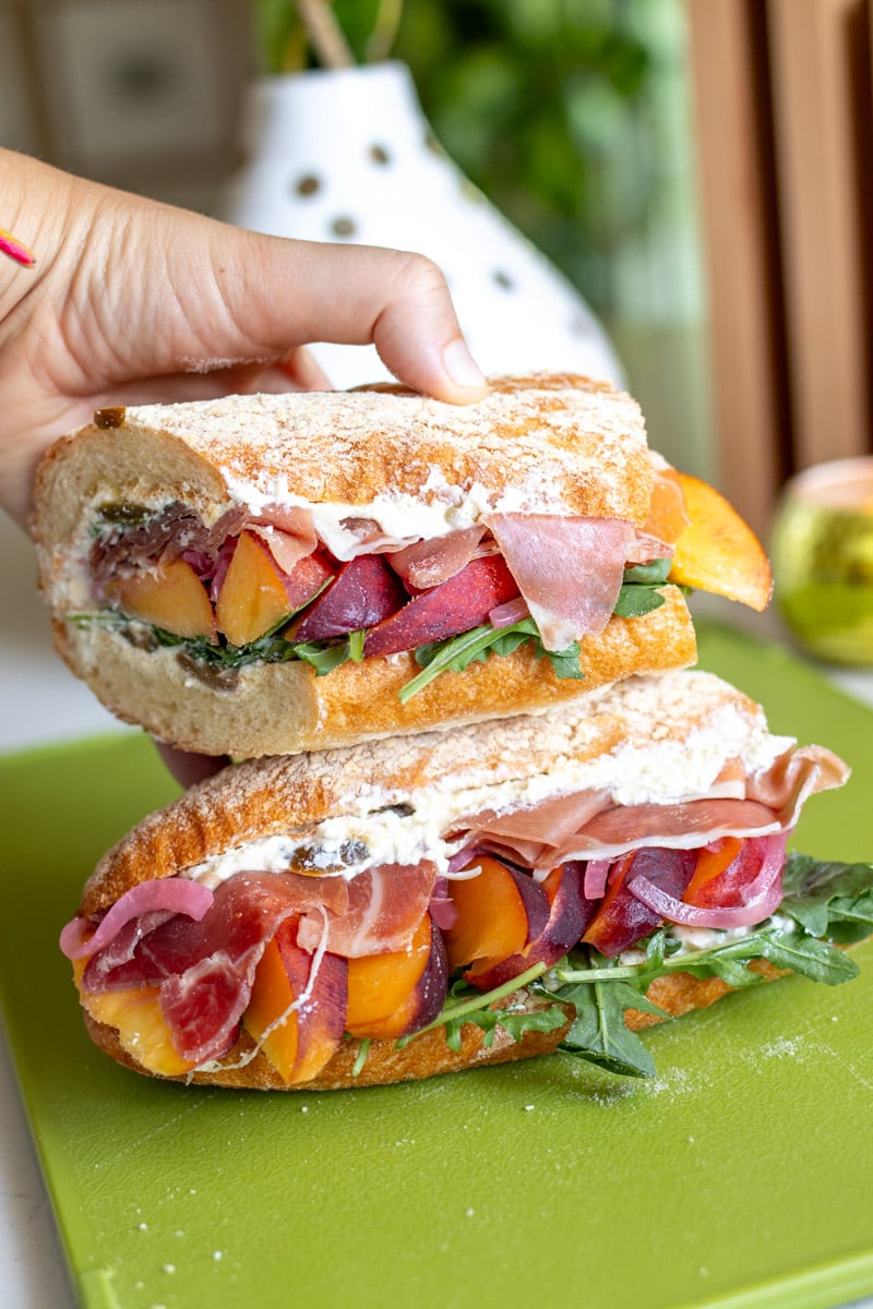 two halves of a prosciutto peach sandwich stacked on top of each other on a green cutting board.