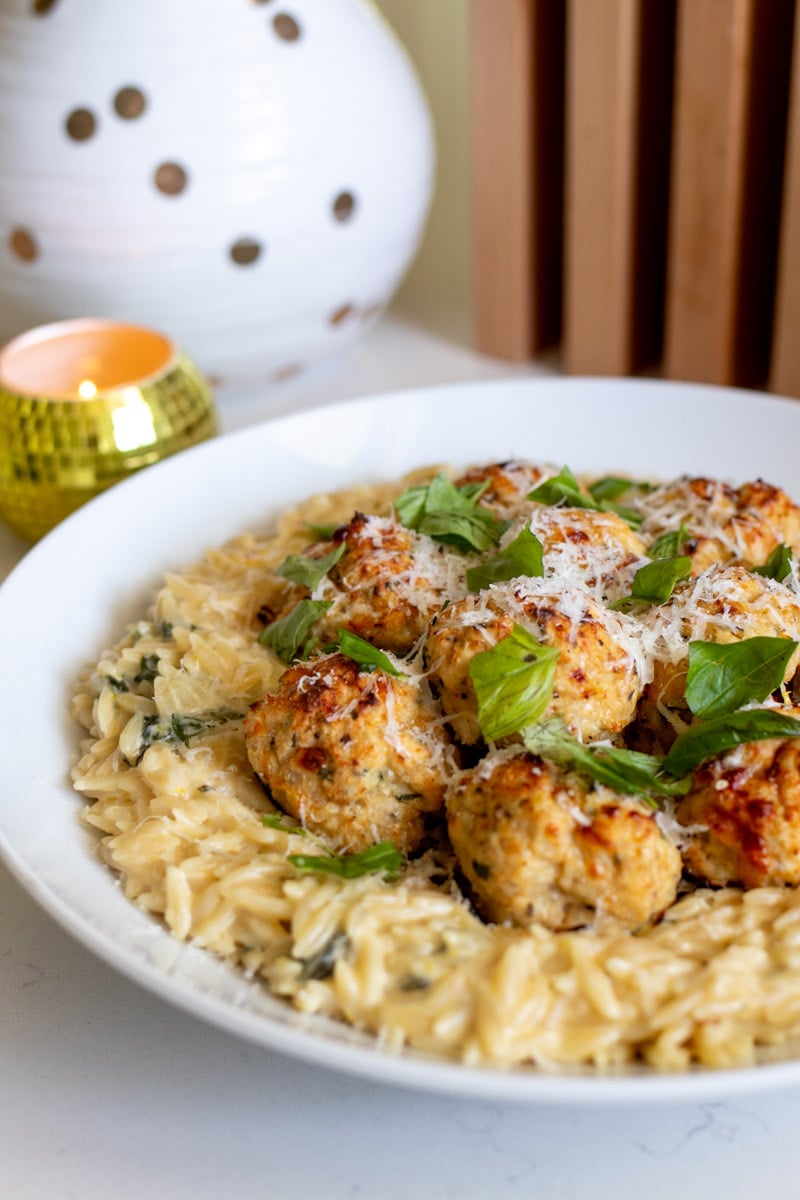 a white bowl full of creamy orzo topped with beatufiul golden chicken ricotta meatballs.