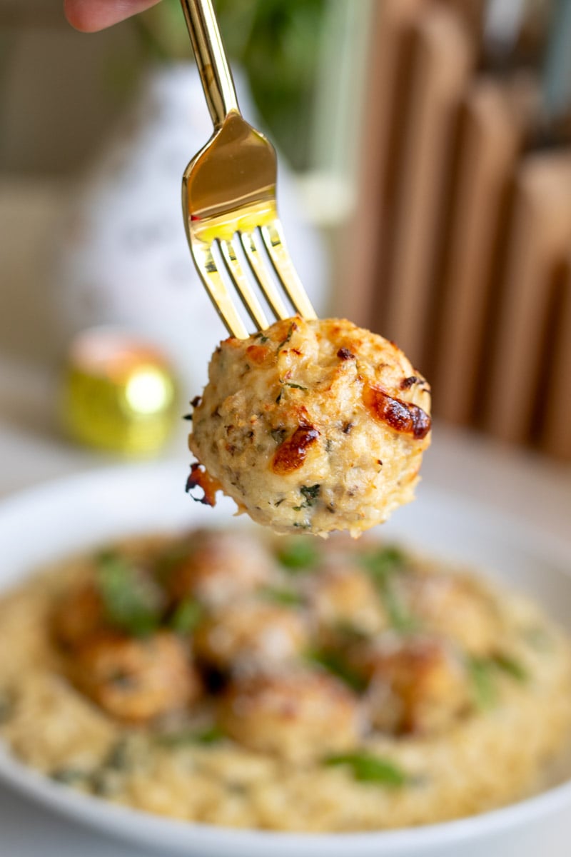 a fork holding a perfectly cooked ricotta chicken meatball over a plate of the orzo.