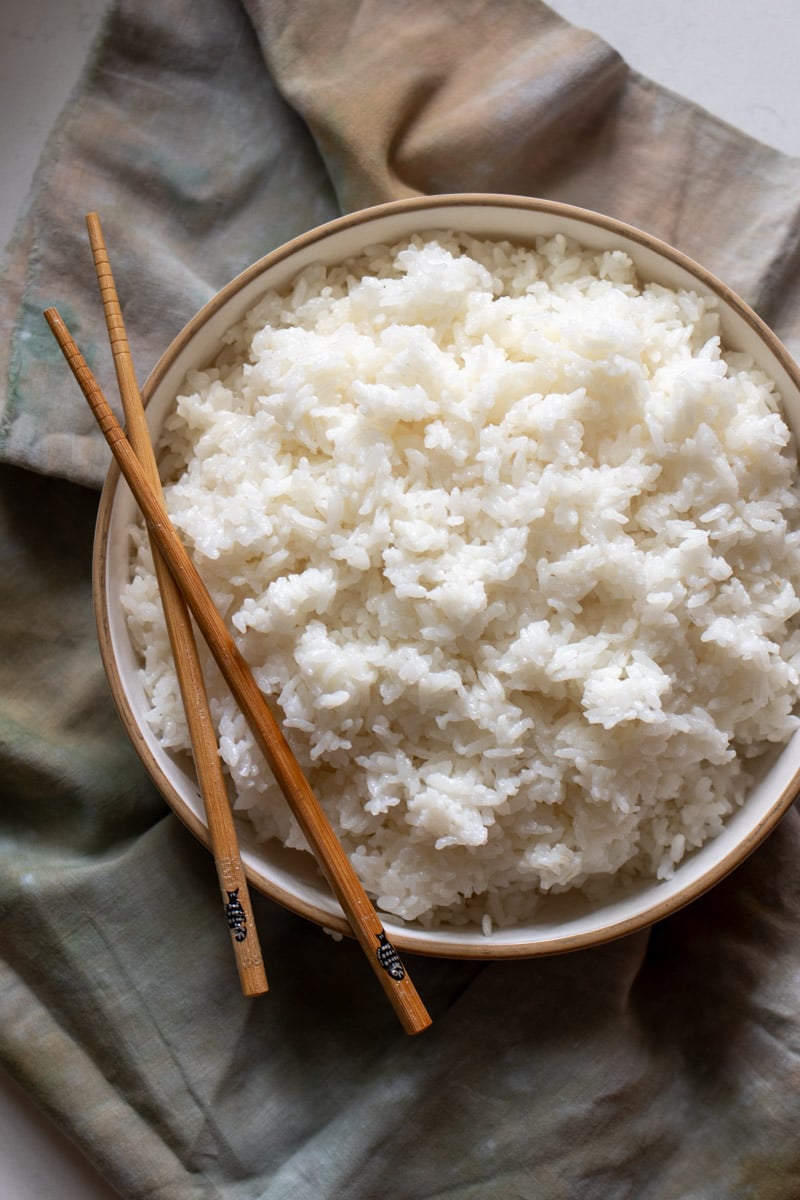 a white bowl of sushi rice with wooden chopsticks on the side on top of a dark napkin.