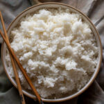 a white bowl of sushi rice with wooden chopsticks on the side on top of a dark napkin.