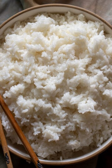 a white bowl of sushi rice with wooden chopsticks on the side on top of a dark napkin.