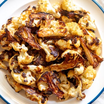 crispy roasted cauliflower on a white plate with a blue rim.