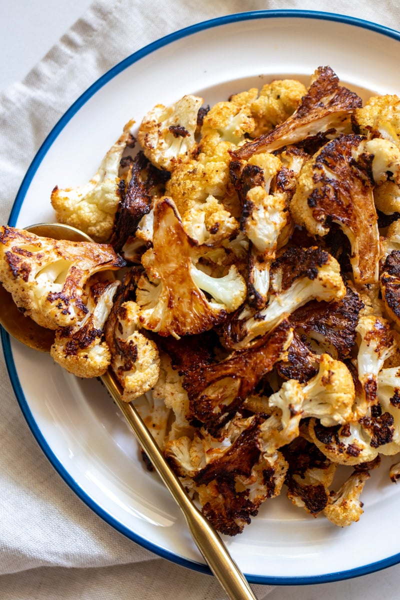 the left side of a white bowl full of crispy roasted cauliflower with golden edges. 