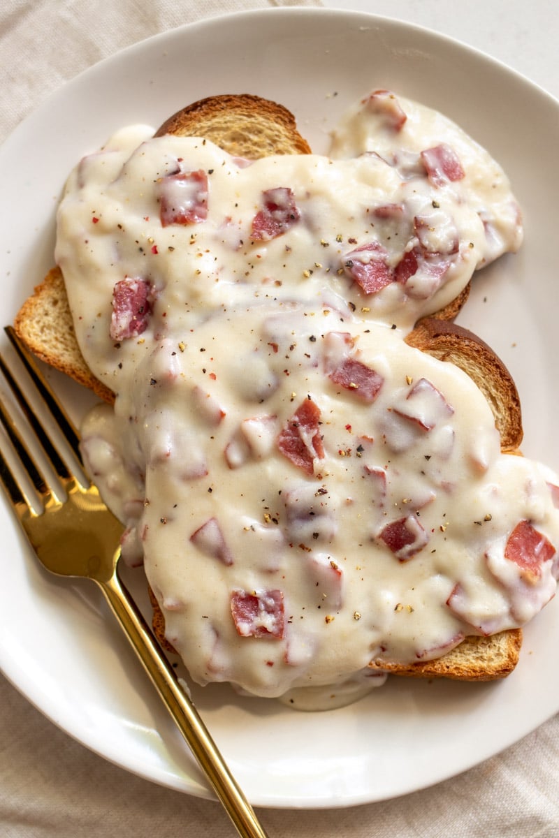 a white plate topped with creamed chipped beef on toast with a golden fork.