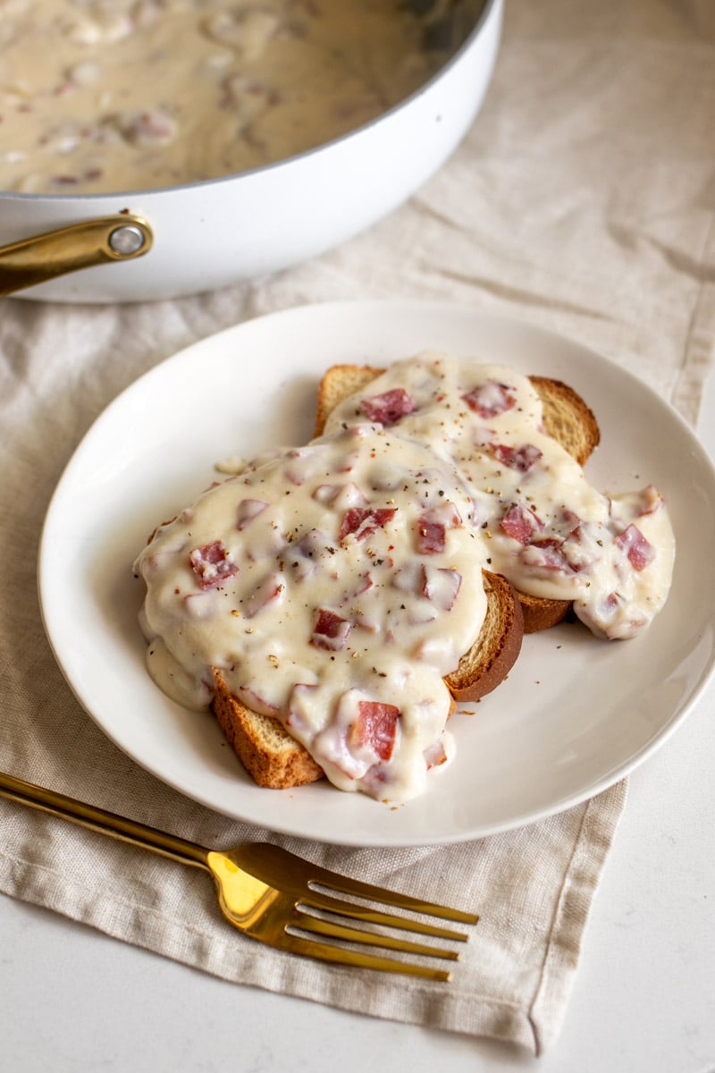 a plate of creamed chipped beef on toast with the pan full of the sauce behind it. 