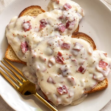 a white plate topped with creamed chipped beef on toast with a golden fork.