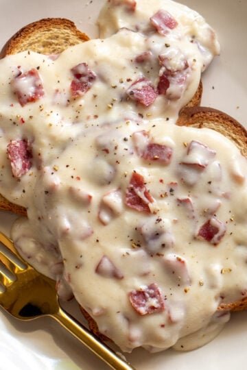 a white plate topped with creamed chipped beef on toast with a golden fork.
