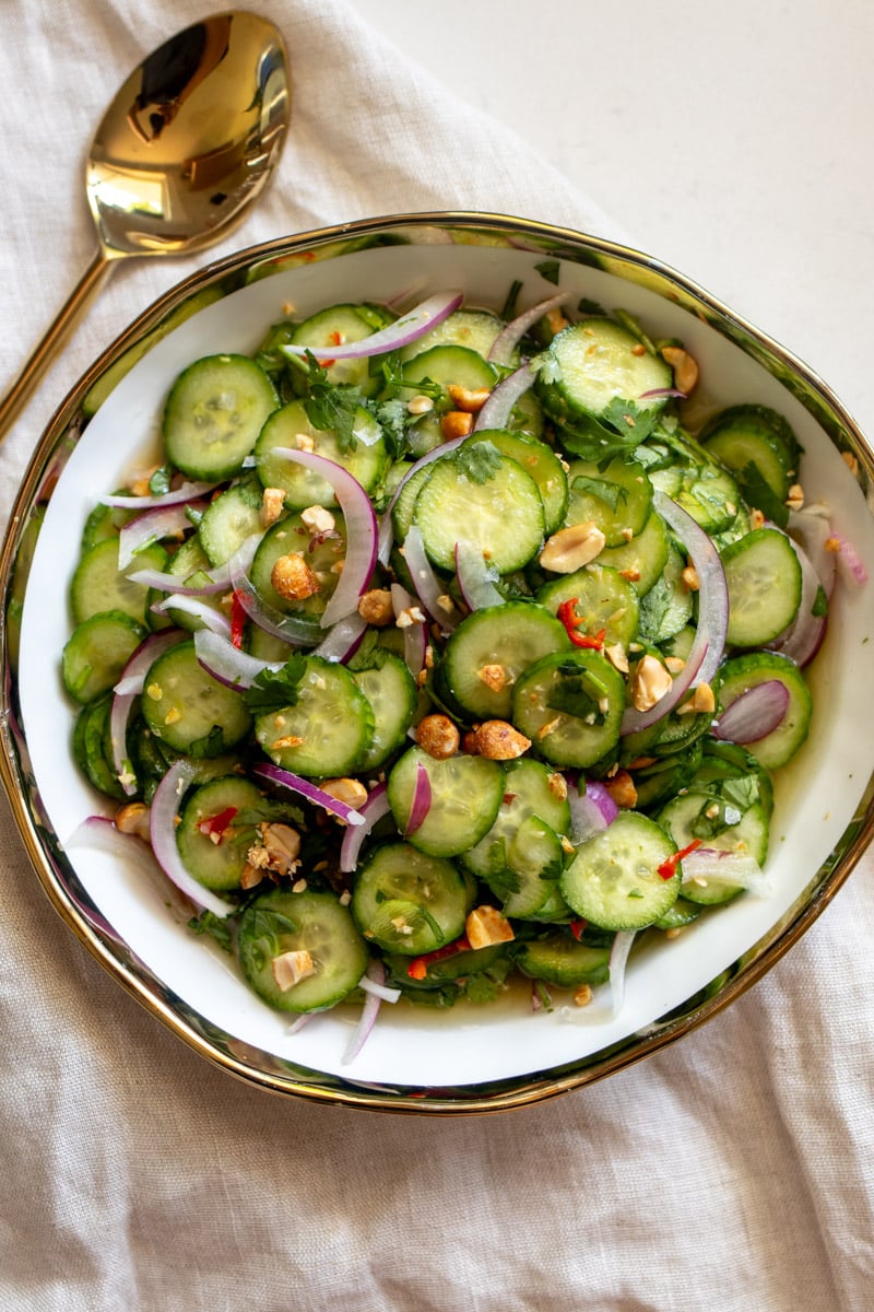 bright green cucumbers, purple onion, red chils and crushed peanuts with vibrant herbs in a white bowl. 