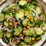 bright green cucumbers, purple onion, red chils and crushed peanuts with vibrant herbs in a white bowl.
