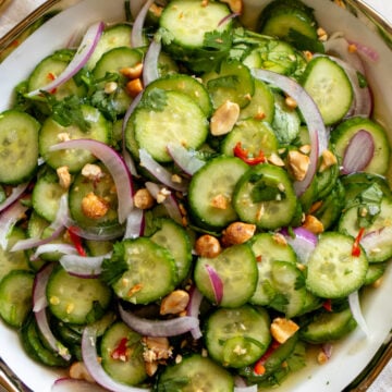 bright green cucumbers, purple onion, red chils and crushed peanuts with vibrant herbs in a white bowl.