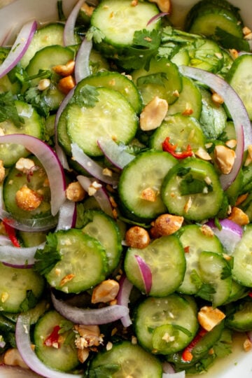 bright green cucumbers, purple onion, red chils and crushed peanuts with vibrant herbs in a white bowl.