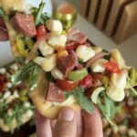 a piece of flatbread with salad and jar-cuterie on top.
