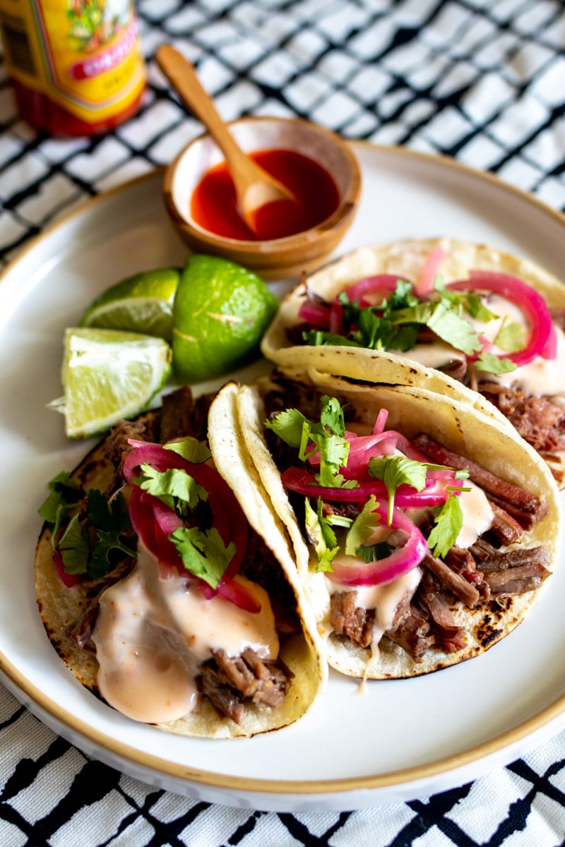 a few shredded beef tacos on a plate with some hot sauce.