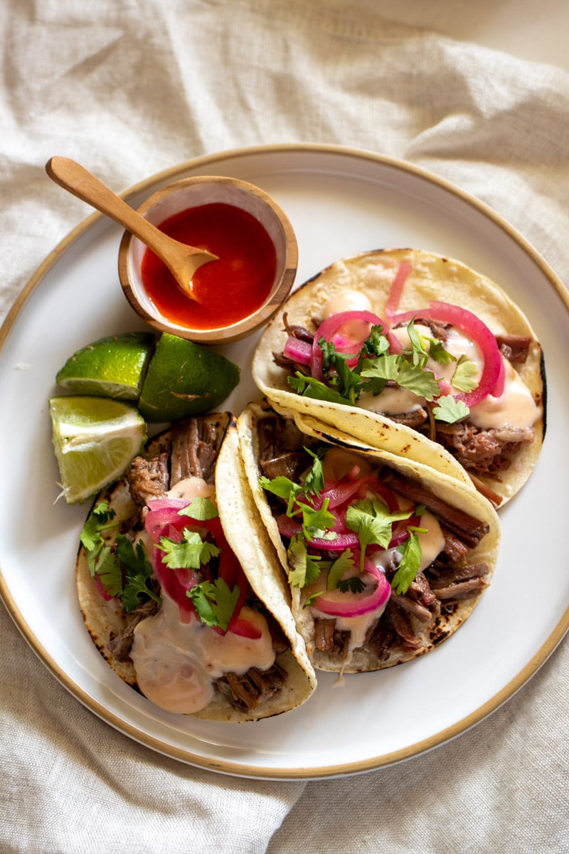 an overhead view of shredded beef tacos with queso dip, pink pickled red onions, and cilantro.
