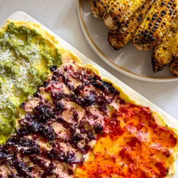 a colorful butter board and grilled corn on a white plate.