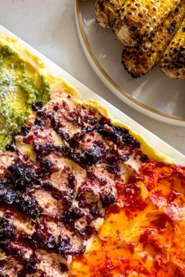 a colorful butter board and grilled corn on a white plate.