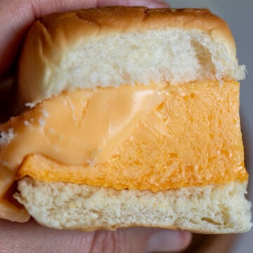 a hand holding a fluffy eggbite breakfast sandwich with melted cheese.