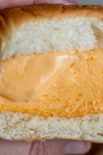 a hand holding a fluffy eggbite breakfast sandwich with melted cheese.