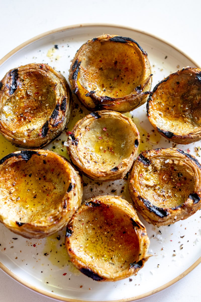 a white plate topped with grilled artichokes and seasoning, lemon and olive oil.