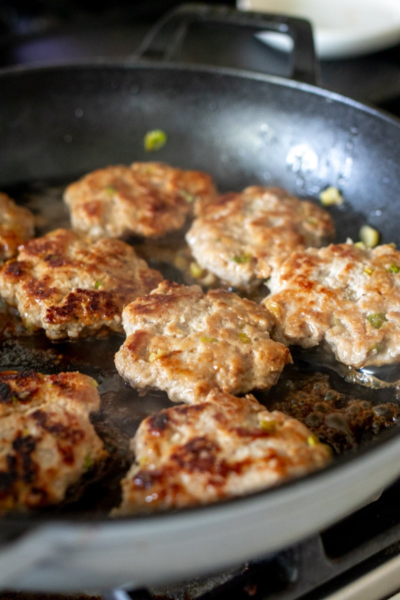 lemongrass turkey sausages pan frying in a large cast iron.