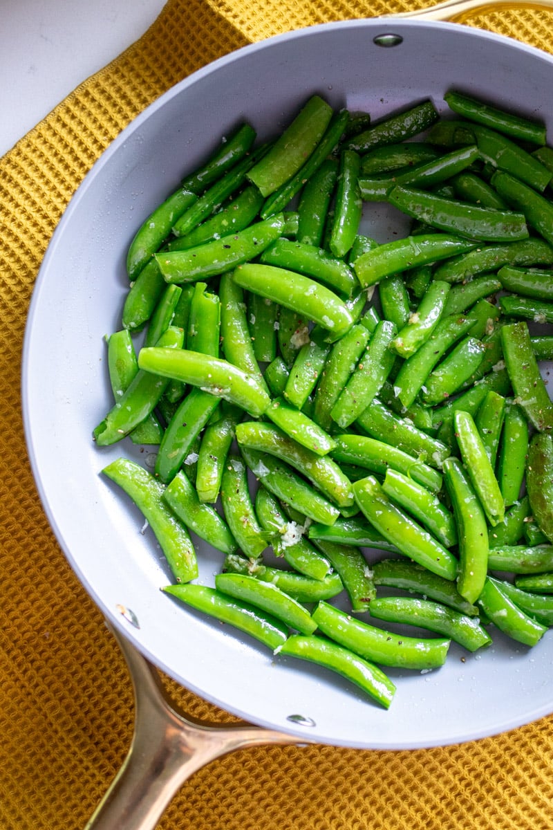 an up close view of the texture of the left side of a white frying pan filled with sugar snap peas.