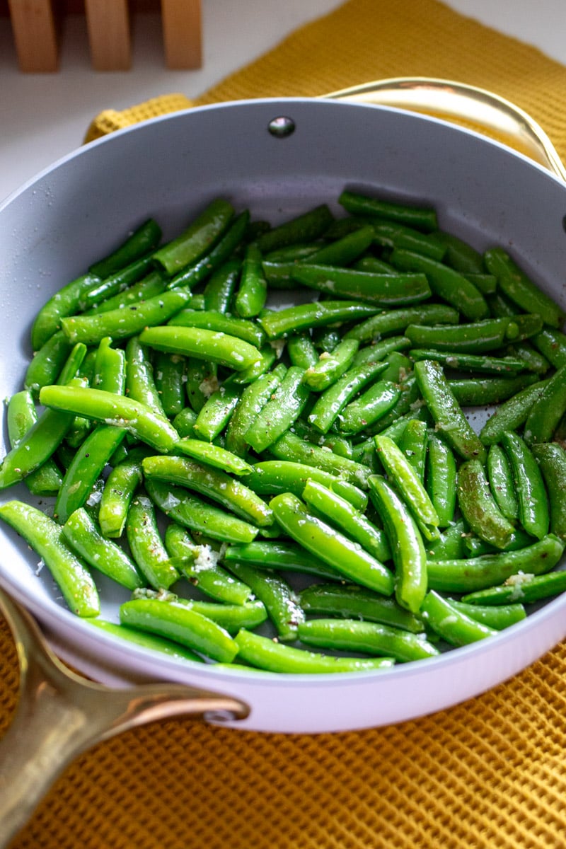 a white saute pan full of bright green tender sugar snap peas.
