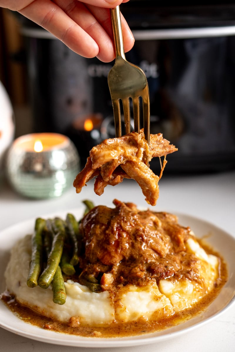 a fork holding super tender crockpot chicken that's been cooked in a golden brown honey mustard sauce.