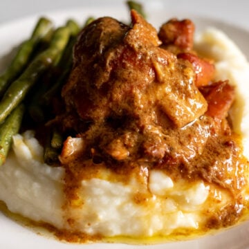 a plate of honey mustard slathered chicken thighs that are fall apart tender with mashed potatoes and green beans.