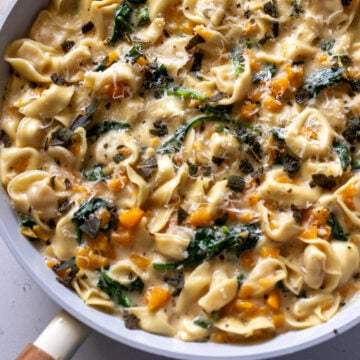 a white pan full of cheese tortellini in a creamy sauce with butternut squash and spinach.