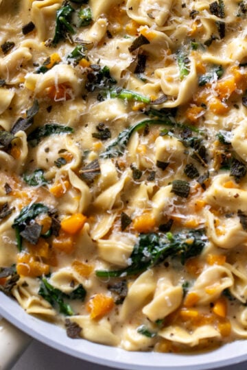 a white pan full of cheese tortellini in a creamy sauce with butternut squash and spinach.