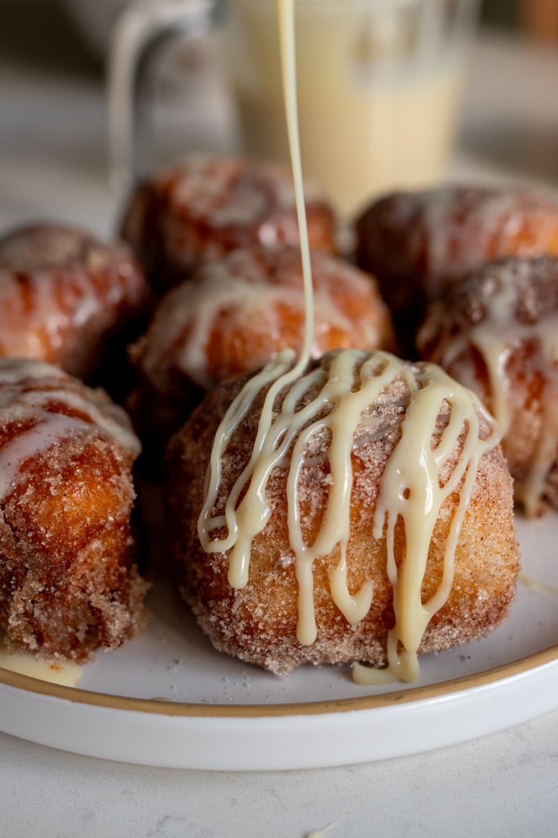sweetened condensed milk being poured over deep fried Hawaiian rolls in a beautiful drizzle.