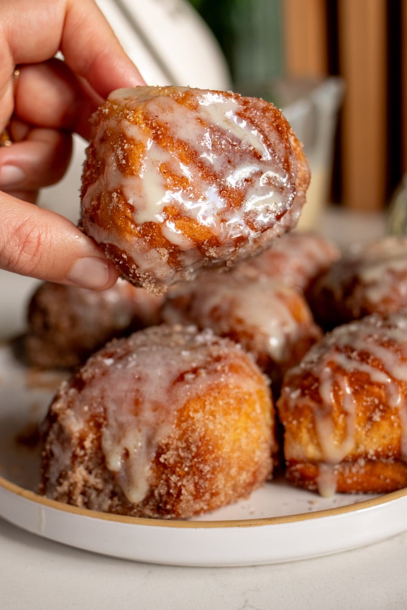 a hand holding a singular deep fried hawaiian roll that's tossed in cinnamon sugar and drizzled with sweetened condensed milk.