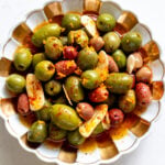 a white and gold bowl full of colorful marinated olives.