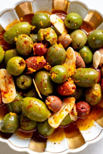 a white and gold bowl full of colorful marinated olives.