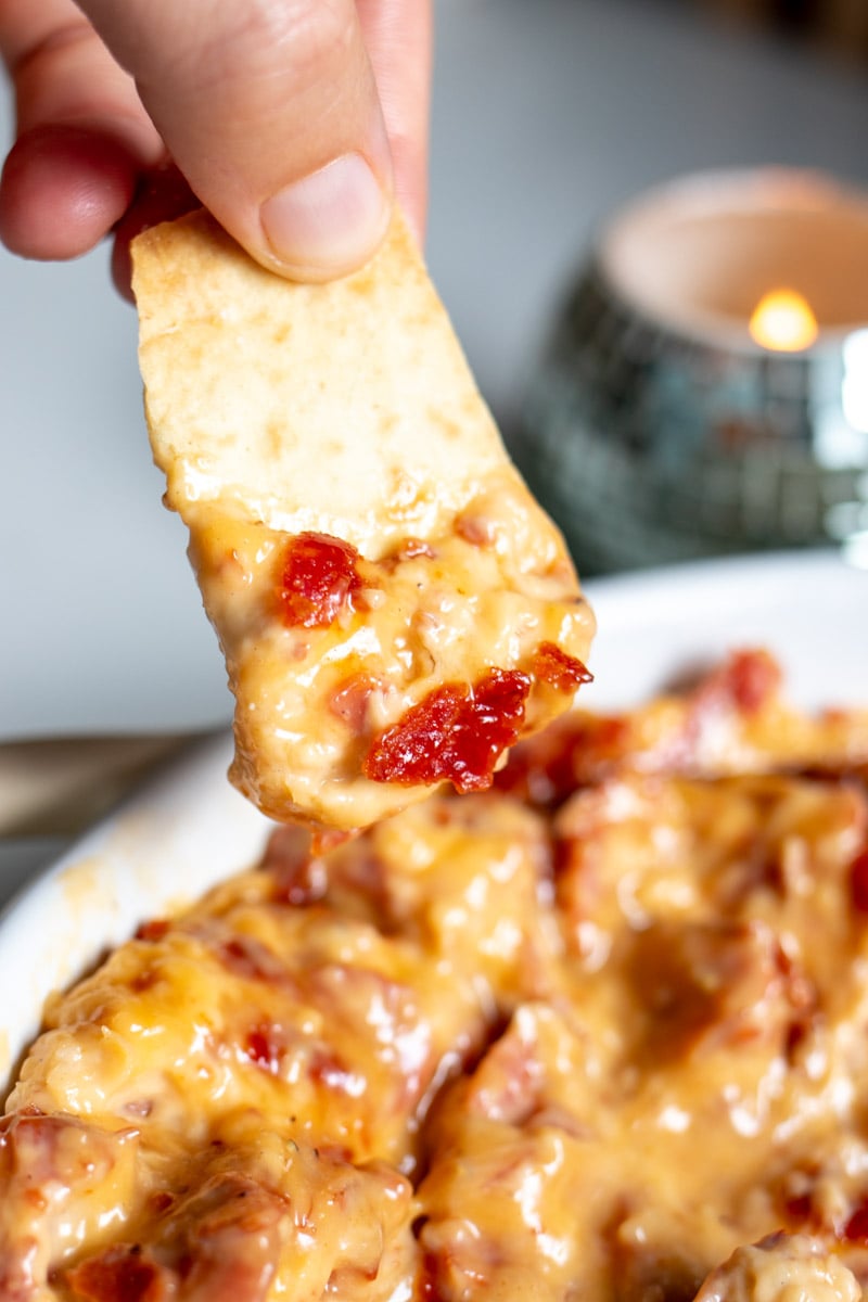 a hand holding a firehook cracker dipping it into this creamy caesar pepperoni dip.