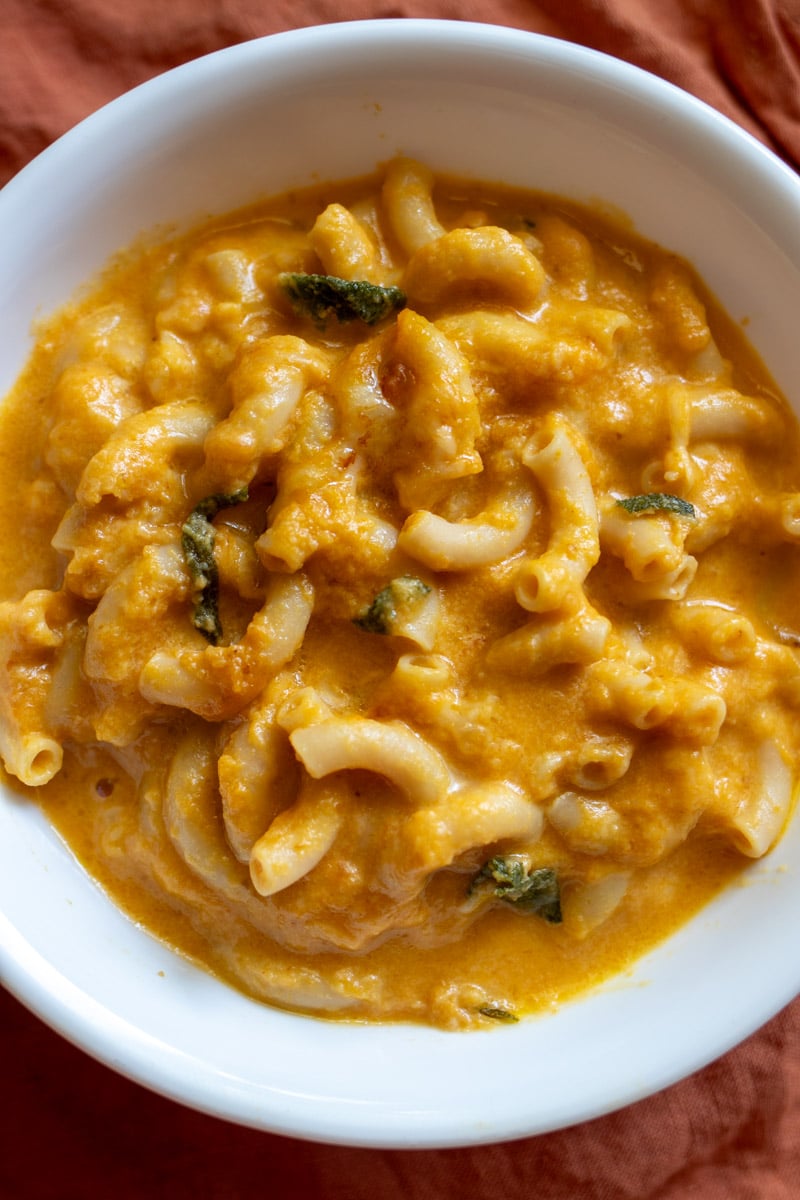 pumpkin mac and cheese in a white bowl with a golden spoon.