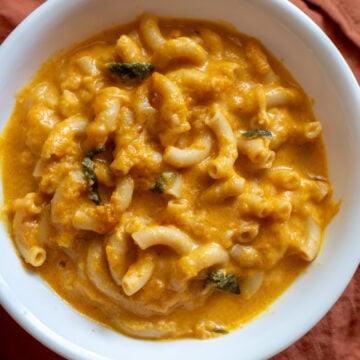 a white bowl filled with orange pumpkin mac and cheese with bits of sage.