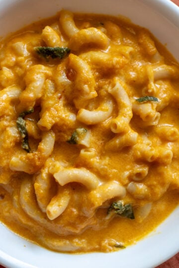 a white bowl filled with orange pumpkin mac and cheese with bits of sage.