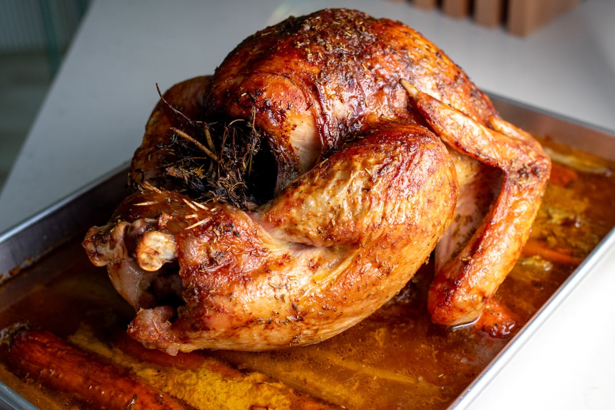 a beautiful roasted turkey with butter and herbs sitting in a roasting pan.