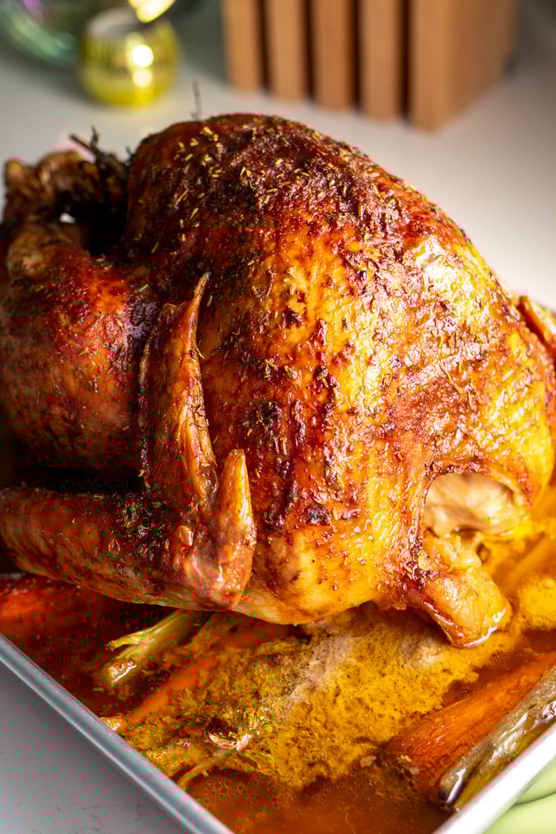 the most beautiful golden roasted turkey that has a buttery herb crust on a white countertop.