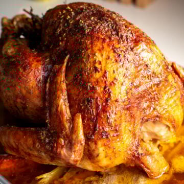 a beautiful thanksgiving turkey that's golden brown and super juicy laying on a bed of roasted vegetables in a roasting pan.