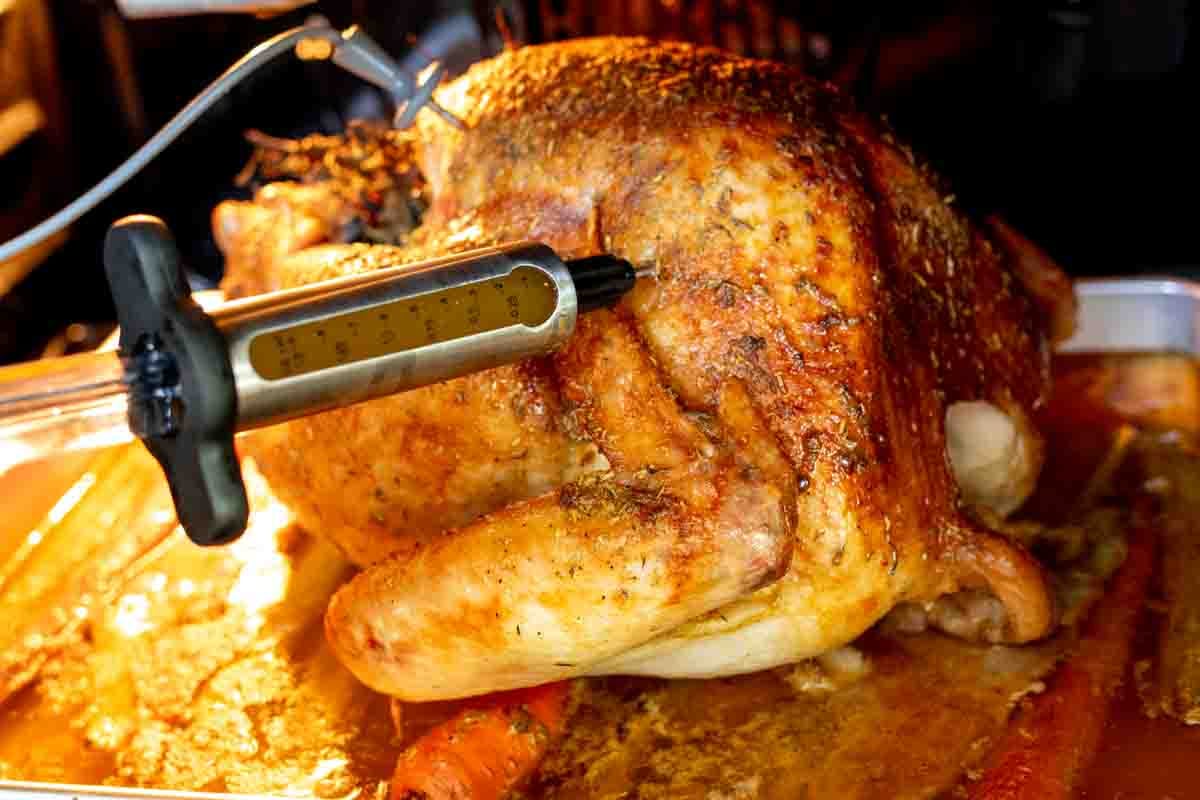 a beautiful golden brown turkey being injected with a flavorful butter mixture.