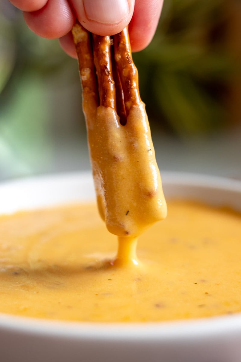 a close up of pretzels being dipped into a creamy orange beer cheese dip. 