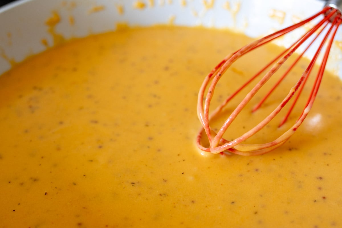 beer cheese dip being whisked together in a sauce pan on a stovetop burner.