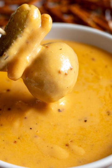 a pickle, pretzel, potato skewer being dipped into creamy beer cheese dip that's made with cheddar and lager.