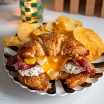 a chicken salad croissant sitting on a black and white plate with chips behind it.