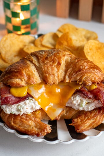 a chicken salad croissant sitting on a black and white plate with chips behind it.