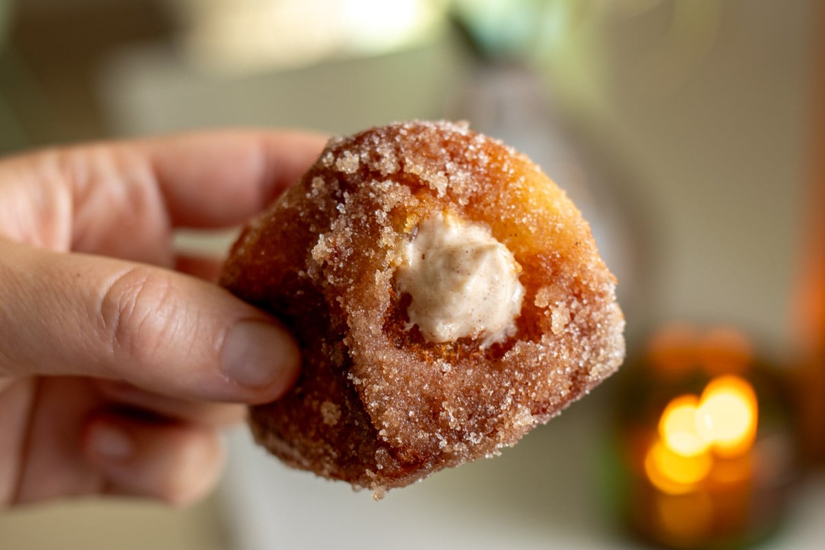 a hand holding a singular pumpkin spice donut that's stuffed with spiced cream cheese.